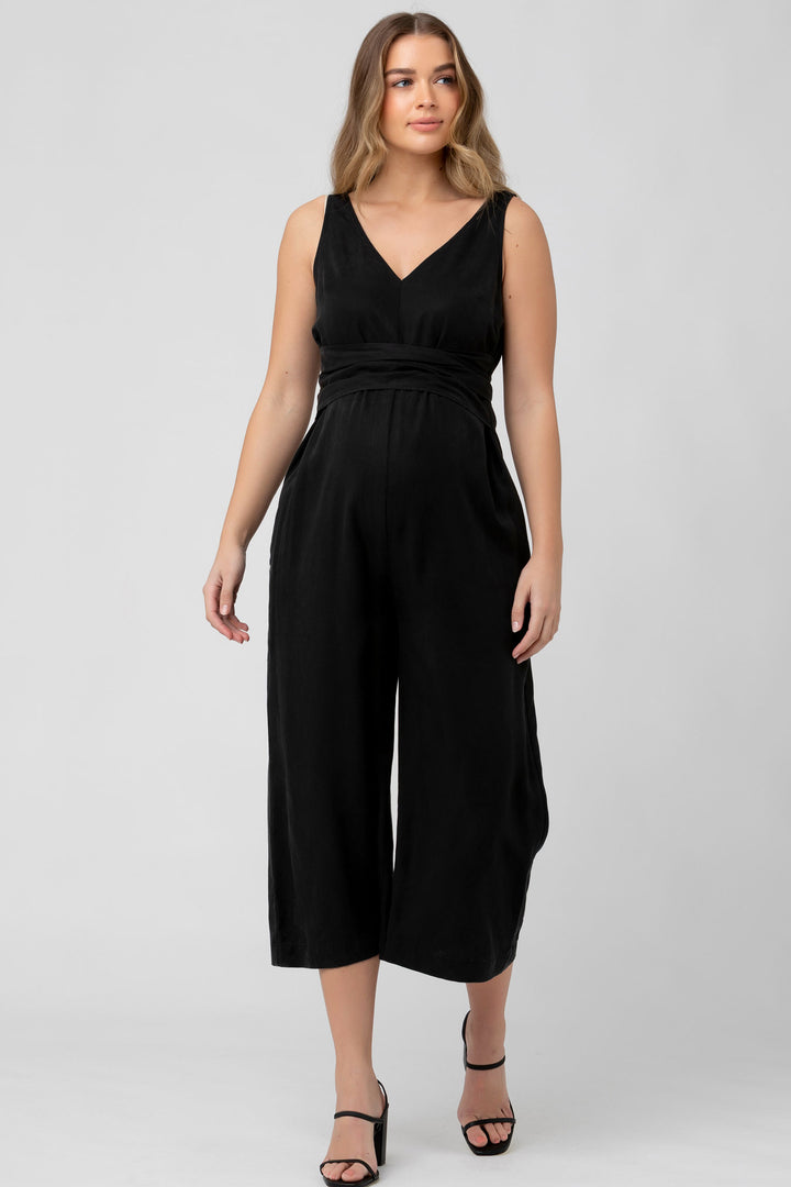 A pregnant woman wearing a black sleeveless V-neck jumpsuit with a tie waist and wide-leg pants.